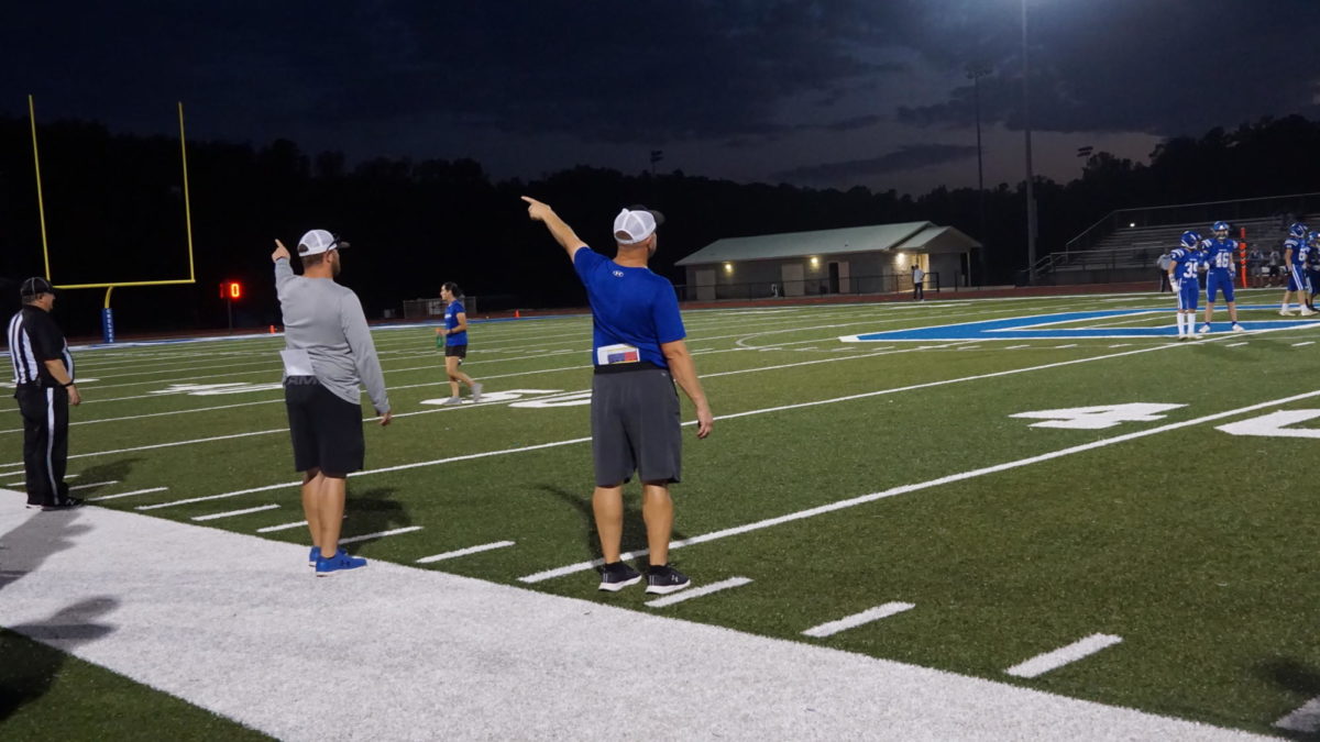 Coach Cassity (right) and Coach Holmes make the same gesture for the boys on the field to initiate a move 